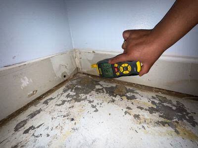 moisture meter testing a wall corner with baseboard and floor covering removed, Woodbridge VA